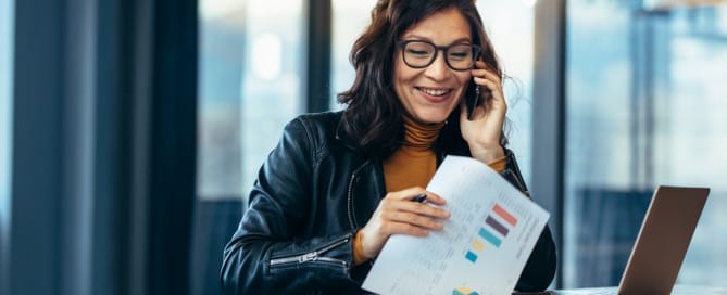 A business woman smiles while speaking on the phone with her accountant.