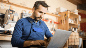 A small business owner works on a laptop in his workshop.